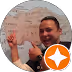 Smiling man gesturing with his hand, with an orange badge featuring a white star in front of him.